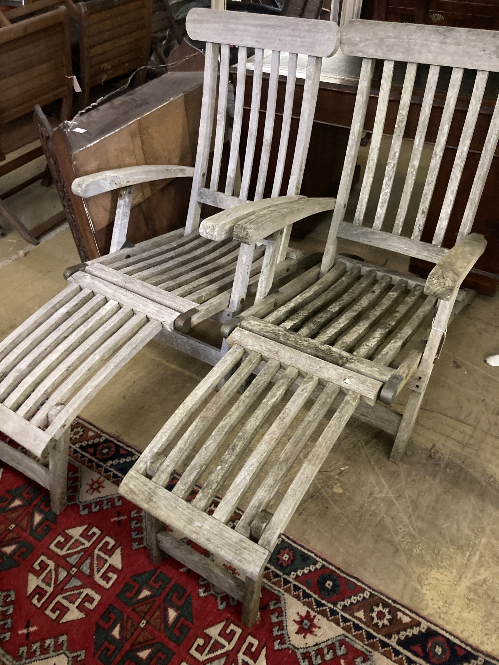 A pair of weathered teak steamer garden chairs with cushions